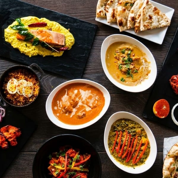 Overhead view of a variety of Indian dishes, including curries, naan, tandoori chicken, and rice.
