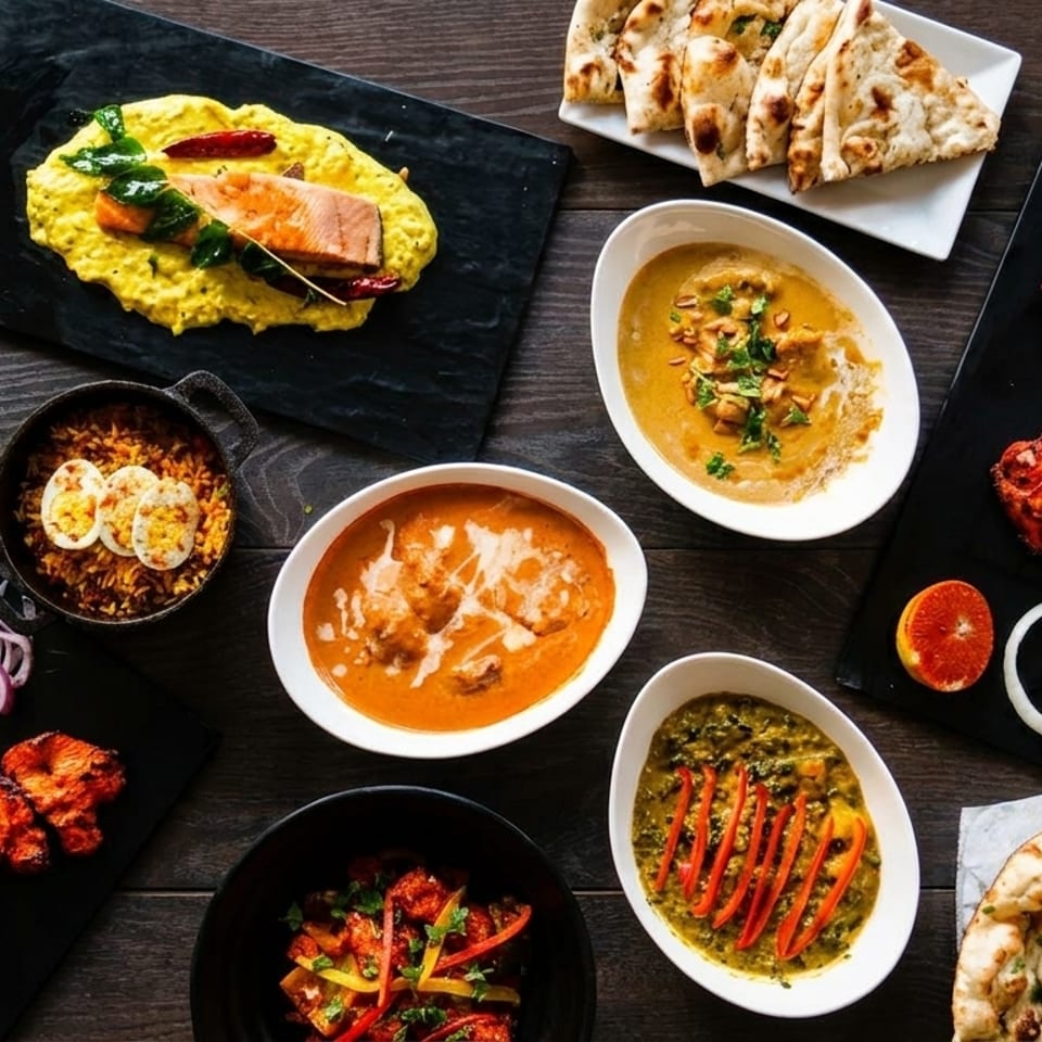 Overhead view of a variety of Indian dishes, including curries, naan, tandoori chicken, and rice.