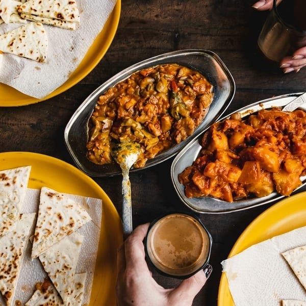 Overhead view of Indian food, including curries, flatbread, and chai, on a wooden table.