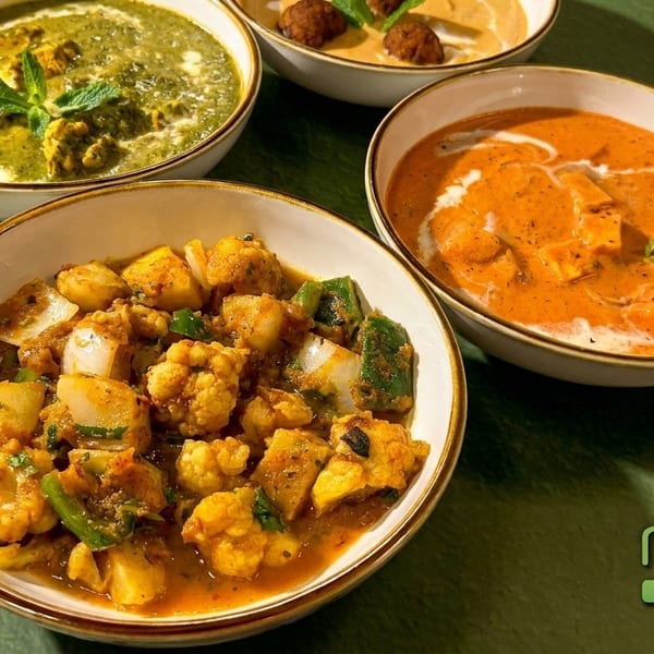 Four bowls of Indian cuisine, including green palak paneer, orange butter chicken, and vegetable curry.